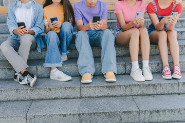Cropped picture of group teenagers holding mobile phones watching video, communication online, chatting sitting on the street. Technology, social media concept - obrazy, fototapety, plakaty
