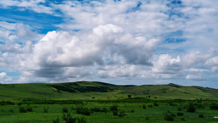 Fototapeta premium Photo of the steppe in summer, with beautiful clouds in the blue sky, the endless steppe at the foot of high hills under a warm summer sky. Khakassia, Siberia, Russia.