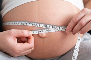 Pregnant girl measures her belly with a measuring tape