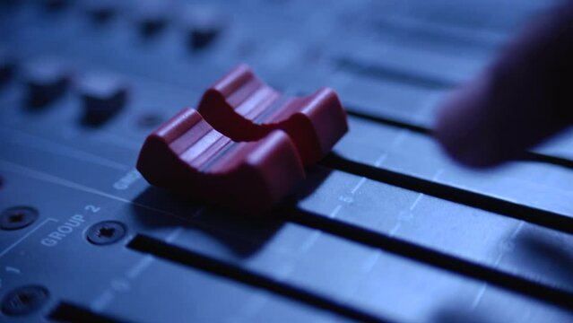 hand turning up volume control on professional mixing console, close shot