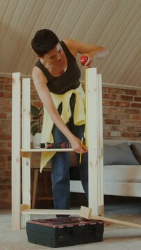 A young woman in casual clothes assembles a rack at home using a tape measure