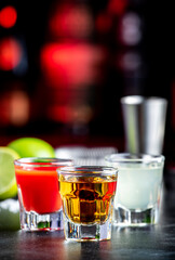 Golden tequila with sangrita and lime juice. Black bar counter background, steel bar tools and bottles