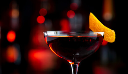 Adonis alcoholic cocktail drink with sherry and red vermouth, black bar counter background, steel tools and bottles
