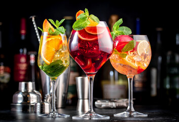 Red, white, rose sangria summer alcoholic cocktail drinks with spanish wine, fruits, citrus and ice. Black bar counter background, steel bar tools and bottles