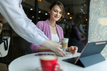 Waiter serve coffee to business woman in cafe. Caucasian female entrepreneur working on a laptop in restaurant on lunch break.