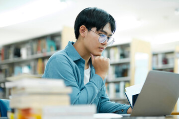 Young university student using laptop for online learning, searching and learning at library.