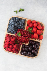 Assorted ripe and juicy berries on a wooden menagerie on a gray table. 