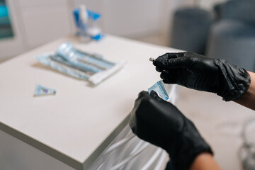 Close-up hands of unrecognizable female dentist in rubber gloves opening package with new nozzle...