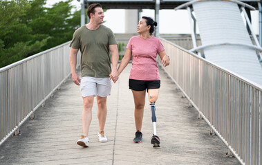 Exercise Asia woman with prosthetic leg holding hand caucasian boy friend in the park city	