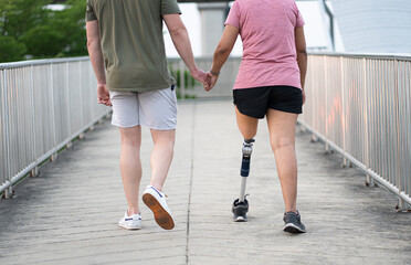 Low angle exercise Asia woman with prosthetic leg holding hand caucasian boy friend in the park...