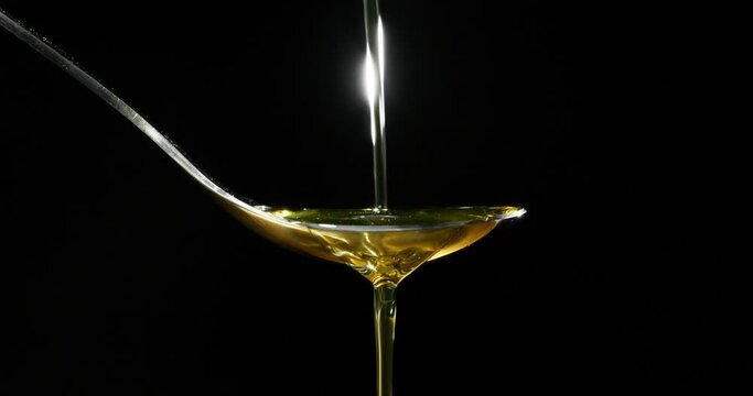 Olive oil pouring on spoon over black background

