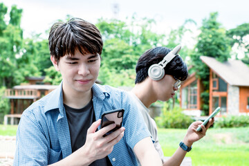 Portrait of young asian gay couple wearing headphones, sitting, listening to music and spending free time together in front of their house, good relationship, LGBT, and best friends concept.
