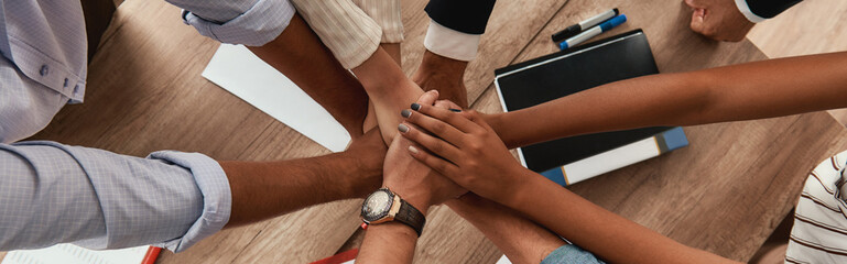 Multicultural team. Top view of business people holding hands together while sitting in the office
