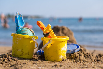 Children's beach toys - buckets, spade and shovel on sand on a sunny day. Bright toys on the background of the sea.