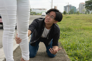 A pitiful young man kneels down and grabs his girlfriend's leg in a desperate attempt to prevent...