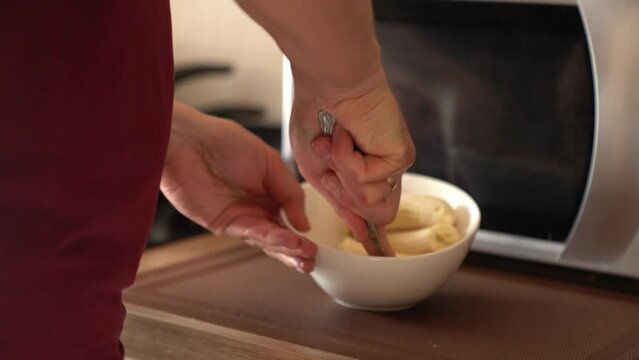 Banana slices in a bowl on the background of the microwave. A man crushes a banana with a fork. Healthy natural puree for baby. High quality 4k footage