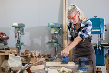 young carpenter caucasian woman using electric wood sander on wood at manufacturing wooden industry. Female craftsman profession in wood factory.