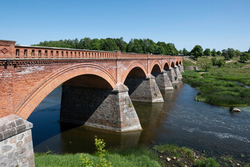 Fototapeta na wymiar The Old Brick Bridge in across the Venta river is the longest bridge of this kind of road bridge in Europe. Kuldīga, Latvia