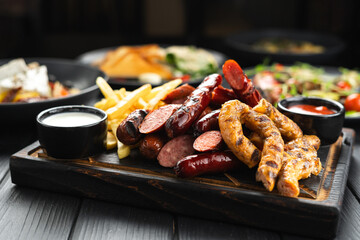 Portion of grilled sausages with baked potato and Prepared Side Dishes Arranged on dark wooden background