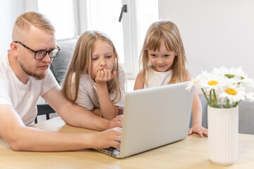Multitasking. Dad and daughters look at the laptop screen, dad explains something to his daughters. Online education, information technology, internet. Family.