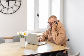 Multitasking. A man speaks on the phone and works on a laptop. Home Office. Work from home.