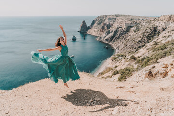 Woman green dress sea. Female dancer posing on a rocky outcrop high above the sea. Girl on the nature on blue sky background. Fashion photo.
