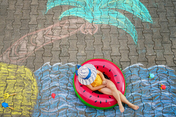 Happy little preschool girl in swimsuit on inflatable ring with sea, sand, palm painted with...