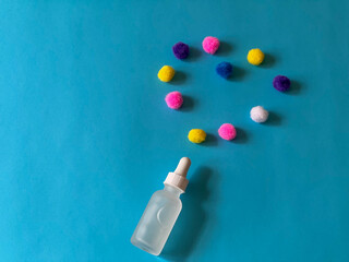 Serum in a glass bottle on a blue background with a multicoloured pom-poms folded in the shape of a heart