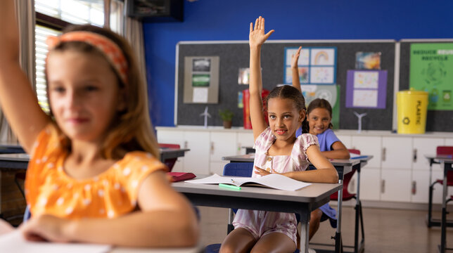 Diverse elementary schoolchildren raising hands at desks in class - Powered by Adobe