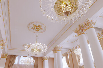 Obraz na płótnie Canvas Beautiful vintage luxury white ceiling with crystal chandeliers and golden stucco. White columns of the wedding palace decorated with stucco.