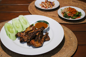 Ayam taliwang or taliwang chicken, a traditional roasted chicken dish from Lombok usually served with beberuk and water spinach plecing. Served with white plate on a wood background
