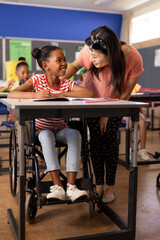 Diverse female teacher and schoolgirl in wheelchair in elementary school class