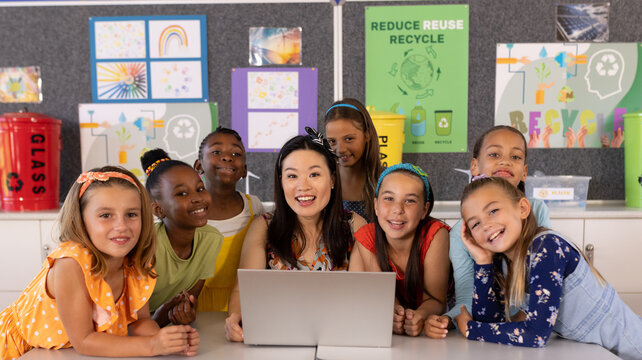 Portrait of diverse female teacher and schoolgirls using laptop in elementary school class