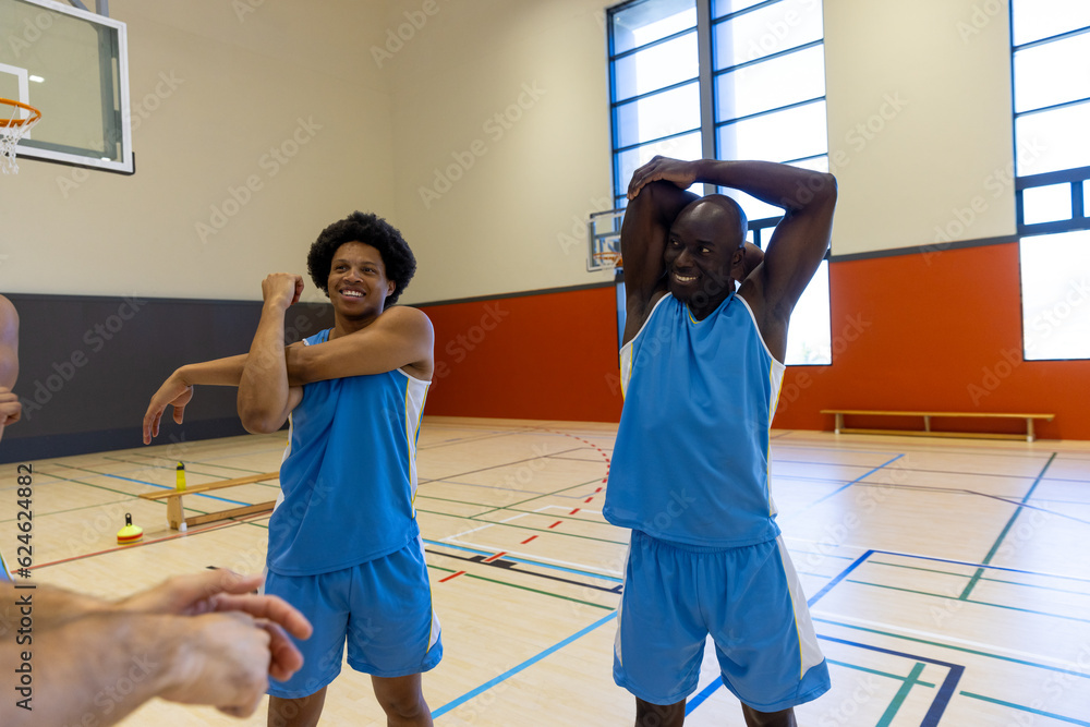 Wall mural happy diverse male basketball players stretching and warming up at gym