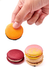 Hand holding orange macarons and 3 colorful macarons (pink, red and cream-brown) isolated on white background. Front side of macaron.