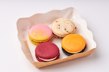 4 colorful macarons (pink, red, orange and cream-brown) placed in a kraft paper food box.