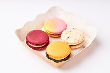 4 colorful macarons (pink, red, orange and cream-brown) placed in a kraft paper food box.