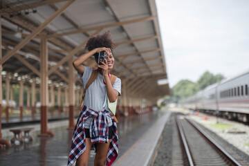 Fototapeta premium Young Asian African woman traveler with backpack in the railway train station, traveler girl walking stand sit waiting take a picture on railway platform train station. High quality photo