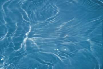 Blue water with ripples on the surface. Defocus blurred transparent blue colored clear calm water surface texture with splashes and bubbles. Water waves with shining pattern texture background.