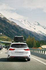 Fototapeta na wymiar White wagon with roof box storage on the highway in Switzerland. Modern family car adventures in the Alpine Mountains in Europe. Plastic luggage compartment on a car roof. Road trip getaway concept.