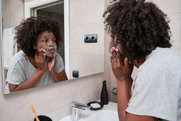 African woman maintains her beauty with daily face washing routine using soap in bathroom.
