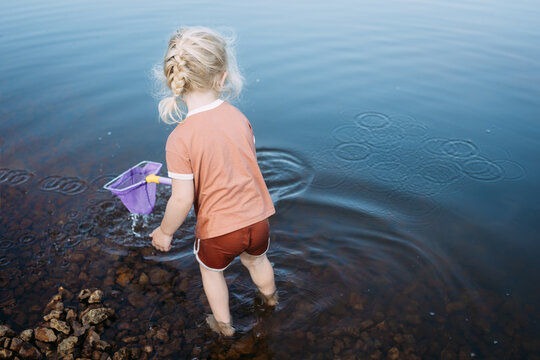 Child on shore dipping fishing net into pond creating water ripp