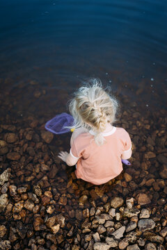 Young girl sitting in water at edge of rocky shore with a fishin