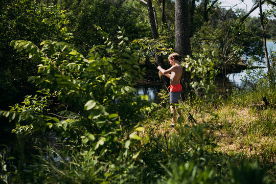 Looking through bushes at boy removing fish from hook on the edg