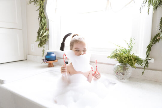 A smiling girl sits in a kitchen sink full of bubbles