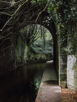 Stone arch tunnel with pathway near river on Camino de Santiago