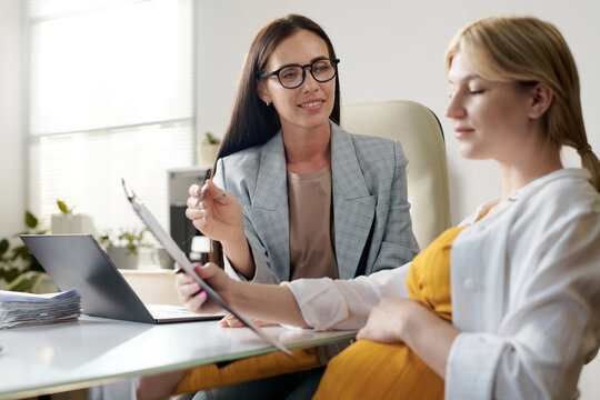 Young social worker giving consultation to pregnant woman during meeting in office