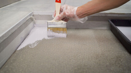 Close-up, paint the floor white with a brush. Applying a white primer to the floor in the room. A hand holds a brush, applying varnish paint on a concrete surface.