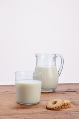 glass jug full of fresh milk with glass of milk and cookies on rustic wooden table