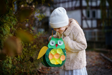 Little preschool kid girl holding selfmade traditional owl lanterns with candle for St. Martin...